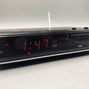 以下が含まれることがあります： 赤いデジタルディスプレイに1:47が表示された、黒いエマーソンFM-AMクロックラジオ。ラジオにはバッテリーバックアップ機能とデュアルアラーム設定があります。