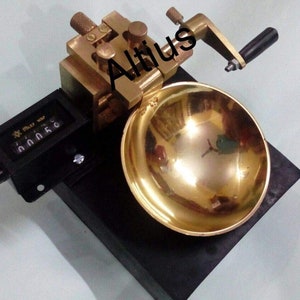 May include: A brass counter with a black base and a gold bowl. The counter has a black digital display with the text "Miley Way" and the number "0.0058". The counter has a black knob and a brass handle with a black knob. The bowl is on a black base.