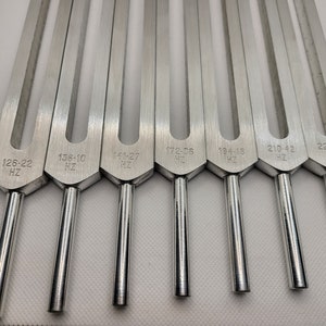 May include: Set of eight silver tuning forks with different frequencies marked on each fork: 128-22 Hz, 136-10 Hz, 141-27 Hz, 172-08 Hz, 194-18 Hz, 210-42 Hz, 221-23 Hz.