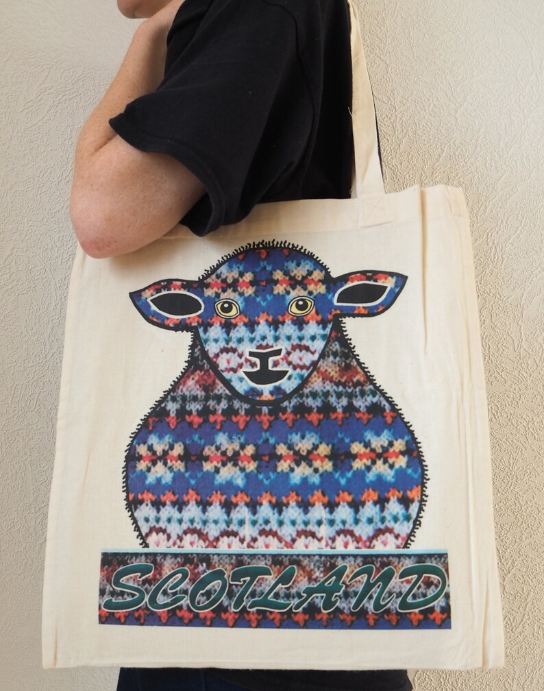 Puede incluir: Una bolsa de lona blanca con un dise&ntilde;o de oveja estampada en azul, rojo y blanco. El texto "SCOTLAND" est&aacute; impreso en verde debajo de la oveja.