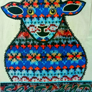 Puede incluir: Una oveja de punto azul, rojo y blanco con contornos negros y ojos amarillos. La oveja est&aacute; de pie sobre un fondo a rayas azul y blanco con la palabra "SCOTLAND" escrita en letras verdes.