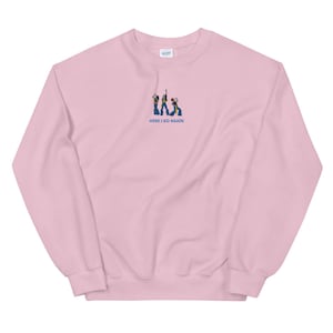 Könnte beinhalten: Rosafarbener Pullover mit einem gestickten Bild von drei Personen in Schlaghosen und dem Text "HERE I GO AGAIN".