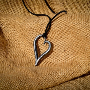 May include: A black cord necklace with a silver heart-shaped pendant. The pendant is made of metal and has a simple, elegant design.