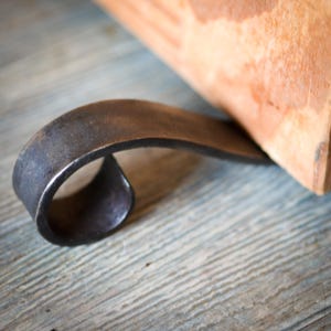 May include: A close-up of a metal doorstop with a curved design. The doorstop is made of dark metal and has a smooth, polished finish.