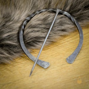 May include: A twisted metal ring with a long metal pin, a traditional style of brooch.