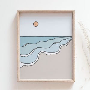 May include: A framed illustration of a beach scene with blue waves crashing on the shore, a light brown sandy beach, and a light orange sun in the sky.