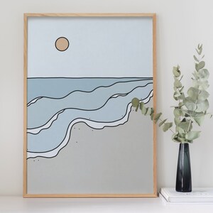 May include: A framed print of a minimalist ocean scene with blue waves and a single yellow sun in a light blue sky. The print is on a light gray background.