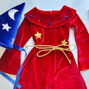 May include: A red velvet wizard costume with a matching blue hat. The costume features a long-sleeved robe with gold star accents and a gold rope belt. The blue hat is decorated with silver crescent moons and stars.