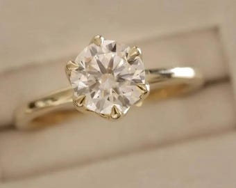 Peut inclure: Une bague de fiançailles en or avec une grosse pierre précieuse ronde et transparente. La bague est sertie dans un sertissage à six griffes, et le bracelet est en or poli. La bague est présentée dans un écrin blanc.