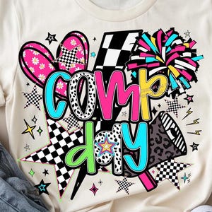 May include: A sublimation design featuring the words "comp day" in colorful letters with a checkered pattern, stars, a lightning bolt, a heart, a megaphone, and a cheerleading pom-pom.