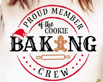 May include: A white sweatshirt with a red circle design that says "Proud Member of the Cookie Baking Crew". A gingerbread man cookie and a rolling pin are inside the circle. The text "CHIKI PUM!" is in a red and yellow speech bubble.