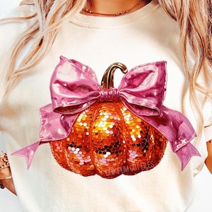May include: A white t-shirt with a pink bow and a sparkly orange pumpkin design. The text "CHIKIPUM CUT FILES" is printed on the pumpkin. The text "ONLY PNG 300 DPI" is printed at the bottom of the image. The text "CHIKI PUM!" is printed in a starburst shape in the bottom right corner of the image.