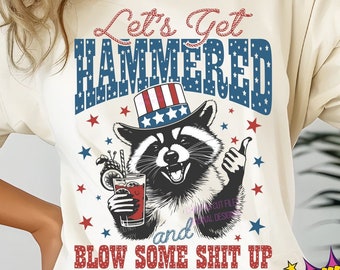 May include: Cream-colored t-shirt featuring a raccoon wearing a patriotic hat and holding a drink. The shirt has the text "Let's Get HAMMERED and BLOW SOME SHIT UP" in red, white, and blue. Stars and a cocktail glass are also visible.