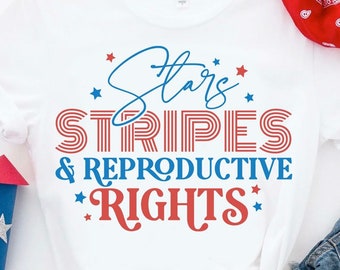 May include: White t-shirt with red and blue text that reads "Stars Stripes & Reproductive Rights". The text is in a retro font style. The shirt is on a white background with a red, white, and blue bandana and a pair of blue jeans in the background.