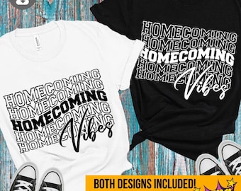 May include: Two white t-shirts with black text that reads "HOMECOMING VIBES" in a stacked, repeating pattern. The text is in a bold, sans-serif font. The shirts are laid out on a wooden surface with a pair of white trainers.