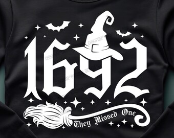 May include: A black long-sleeved shirt with a white graphic design of a witch's hat, the number 1692, a broom, and the text "They Missed One".