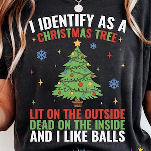 May include: Dark gray t-shirt with the text "I IDENTIFY AS A CHRISTMAS TREE" above a green Christmas tree graphic. The shirt also says "LIT ON THE OUTSIDE DEAD ON THE INSIDE AND I LIKE BALLS".