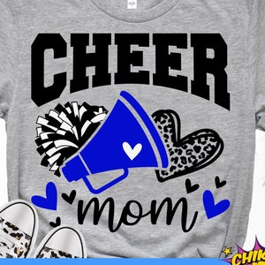 May include: A gray t-shirt with the text "CHEER mom" in black. A blue megaphone with a white heart is next to the text. A black and white pom-pom is behind the megaphone. A leopard print heart is next to the megaphone. There are small hearts around the text.