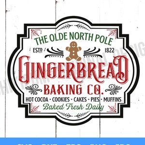 May include: A vintage-style sign with black lettering on a white background. The sign reads "The Olde North Pole Gingerbread Baking Co." with the text "Est. 1822" and "Hot Cocoa, Cookies, Cakes, Pies, Muffins, Baked Fresh Daily" in smaller font. The sign has a gingerbread man graphic in the center.