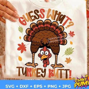 May include: White sweatshirt with a cartoon turkey design. The turkey is brown with a red head and is upside down. The text "GUESS WHAT? TURKEY BUTT!" is in brown and orange. Fall leaves are scattered around the turkey.