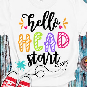 May include: A white t-shirt with the text "hello HEAD start" in colorful letters. The text is surrounded by hearts, paint splatters, and a paper airplane. The words "CHIKI PUM!" are in a speech bubble in the bottom right corner. The image includes the text "SVG + DXF + EPS + PNG + JPG".