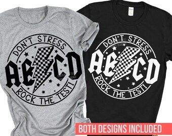 Puede incluir: Dos diseños de camisetas con un gráfico en blanco y negro de un rayo con un patrón a cuadros y el texto "Don't Stress ABCD Rock the Test!" en un círculo.