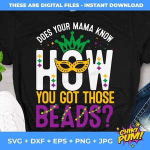 May include: Black t-shirt with the text "DOES YOUR MAMA KNOW HOW YOU GOT THOSE BEADS?" in white, yellow, green, and purple. The design includes a mask and crown, with a pair of jeans and white sneakers in the background.
