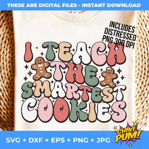 May include: A white t-shirt with a retro-style design that says "I Teach The Smartest Cookies". The design features colourful, rounded letters and gingerbread cookies. The text "CHIKI PUM!" is in a speech bubble in the bottom right corner.