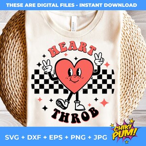 Op de afbeelding: Een wit T-shirt met een rode hartgrafiek met armen en benen. Het hart draagt ​​een geruit patroon en de tekst "HEART THROB" is in zwarte letters geschreven.