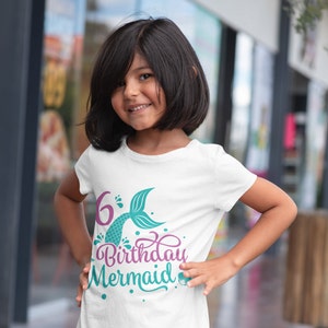 May include: White t-shirt with a colorful mermaid-themed design. The graphic includes the number "6", a mermaid tail, and the words "Birthday Mermaid" in a script font. The shirt is worn by a young girl.