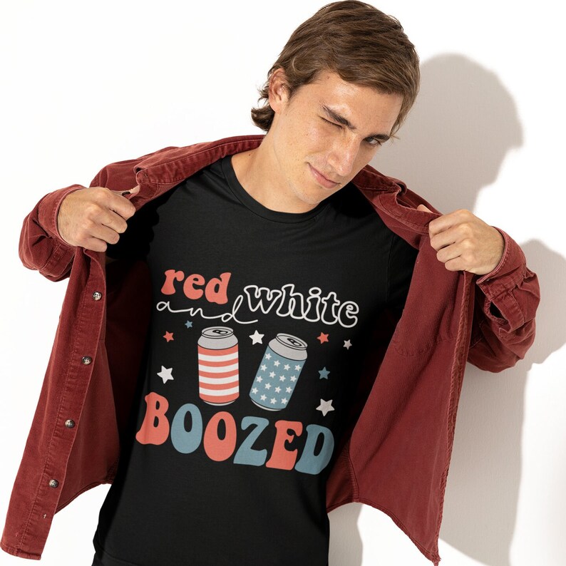Pu&ograve; includere: Una maglietta nera con un design grafico rosso, bianco e blu. Il grafico presenta il testo "red white and boozed" con tre lattine di birra stilizzate.