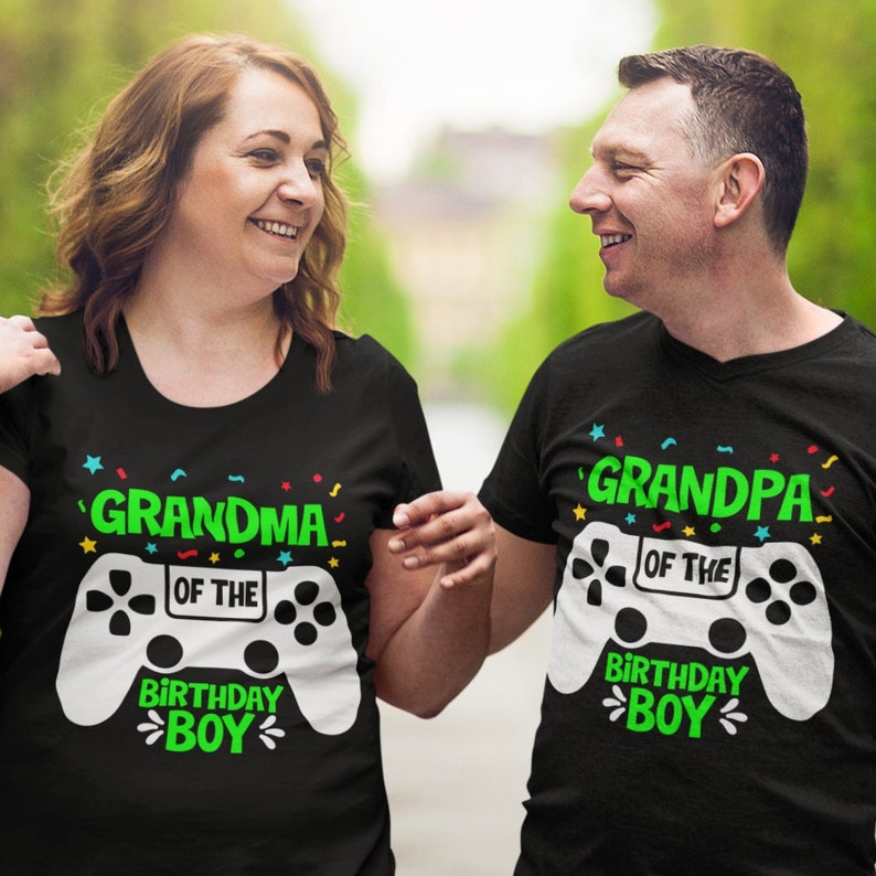 May include: Two people wearing black t-shirts with a white video game controller graphic. The text on the shirts reads "Grandma of the Birthday Boy" and "Grandpa of the Birthday Boy".