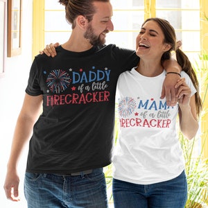 Op de afbeelding: Een stel draagt ​​bijpassende zwarte en witte T-shirts met rood-wit-blauwe vuurwerkgrafieken. De tekst op de shirts luidt "Daddy of a little Firecracker" en "Mama of a little Firecracker".