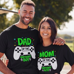 May include: Black t-shirts with a white video game controller graphic and text that reads "Dad of the Birthday Boy" and "Mom of the Birthday Boy".