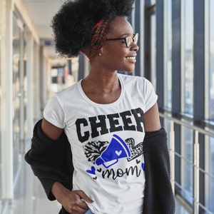 May include: White t-shirt with a black and blue graphic that says "CHEER mom" with a megaphone and pom poms.