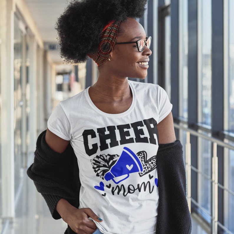 May include: White t-shirt with a black and blue graphic that says "CHEER mom" with a megaphone and pom poms.