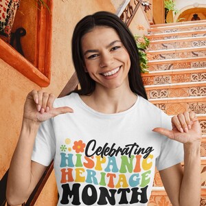 Pode incluir: Uma camiseta branca com um gr&aacute;fico colorido que diz "Celebrating Hispanic Heritage Month". O gr&aacute;fico est&aacute; em um estilo retr&ocirc; com um design de flores.