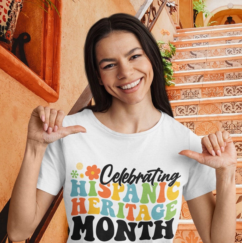 Pode incluir: Uma camiseta branca com um gr&aacute;fico colorido que diz "Celebrating Hispanic Heritage Month". O gr&aacute;fico est&aacute; em um estilo retr&ocirc; com um design de flores.