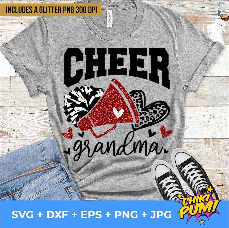K&ouml;nnte beinhalten: Ein graues T-Shirt mit dem Text "CHEER grandma" in Schwarz. Neben dem Text befindet sich ein rotes Glitzer-Megafon mit einem wei&szlig;en Pompon. Das Design ist perfekt f&uuml;r eine Cheerleader-Oma.
