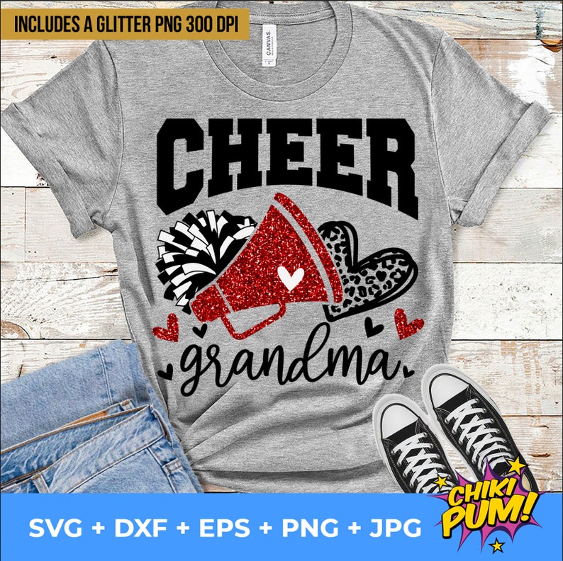 K&ouml;nnte beinhalten: Ein graues T-Shirt mit dem Text "CHEER grandma" in Schwarz. Neben dem Text befindet sich ein rotes Glitzer-Megafon mit einem wei&szlig;en Pompon. Der Text "CHIKI PUM!" befindet sich in einer Sprechblase unten rechts.