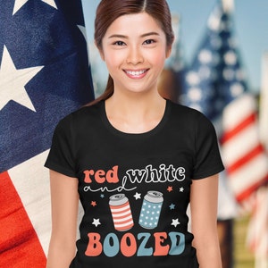 Pu&ograve; includere: Una maglietta nera con il testo "red white and boozed" in lettere bianche e rosse. Due lattine di birra cartoon con strisce rosso, bianco e blu sono accanto al testo.