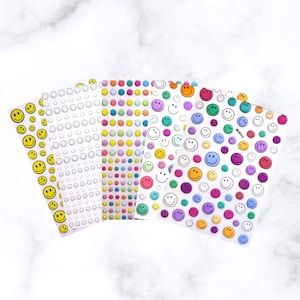 May include: Four sheets of stickers with smiley face designs. The sheets feature various colors, including yellow, pink, green, purple, and blue. Some sheets have solid-colored smiley faces, while others have outlines or a mix of colors.