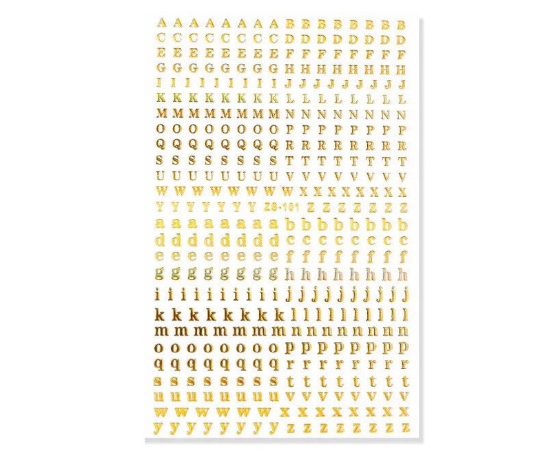 May include: Gold metallic alphabet letter stickers on a white background. The stickers include uppercase and lowercase letters, numbers, and symbols. The letters are in a sans-serif font and are arranged in rows and columns.