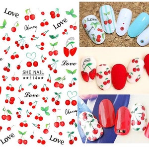 May include: A sheet of nail art stickers featuring red cherries, green leaves, and the word "Love" in black. Several nail designs with cherry patterns are also shown, including solid red and white nails with cherry decals.