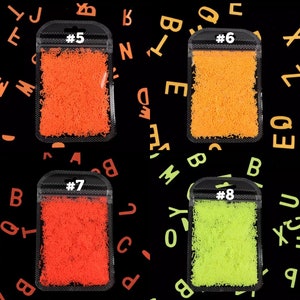 May include: Four small plastic bags filled with colorful, shredded material. The bags are labeled with the numbers 5, 6, 7, and 8. The background is black with scattered orange and green letters.