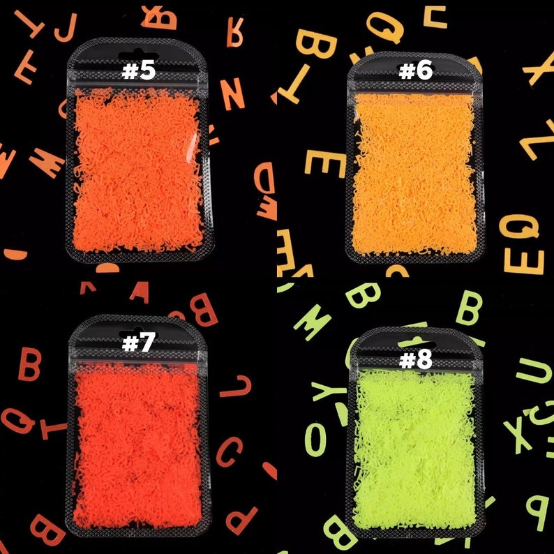May include: Four small plastic bags filled with colorful, shredded material. The bags are labeled with the numbers 5, 6, 7, and 8. The background is black with scattered orange and green letters.