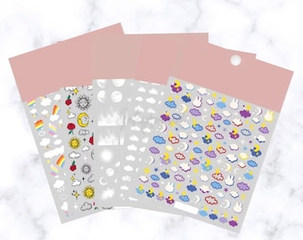 May include: Four sheets of decorative stickers with celestial and whimsical designs. Each sheet features a different pattern, including rainbows, suns, moons, clouds, and stars. The stickers are in various colors, including red, yellow, blue, and purple.