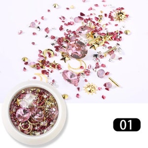 May include: A collection of nail art supplies, including pink and clear rhinestones, gold star and moon charms, and a small container filled with similar embellishments. The number "01" is displayed in a black rectangle.