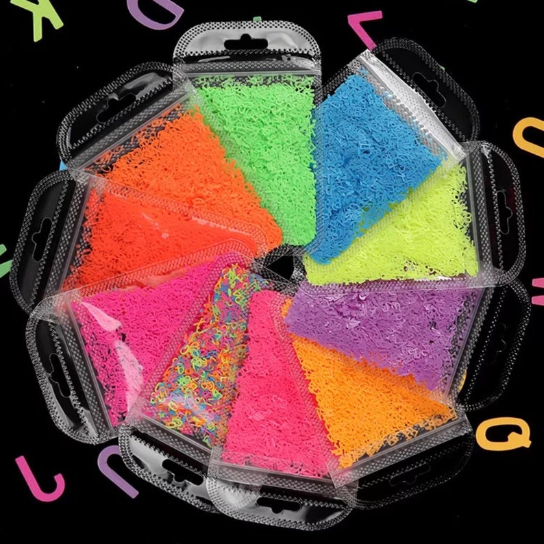 May include: A collection of colorful craft supplies in clear plastic bags. The assortment includes neon green, orange, pink, purple, and blue materials. The bags are arranged in a circular pattern against a black background.