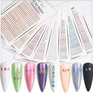May include: Nail art stickers with various letters and designs. The image shows multiple sheets of small alphabet stickers in different colors, along with several painted nail tips with letters and words like "LOVE" and "GIF".